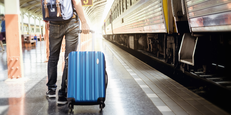 Un homme se tient à la gare avec une valise à roulettes